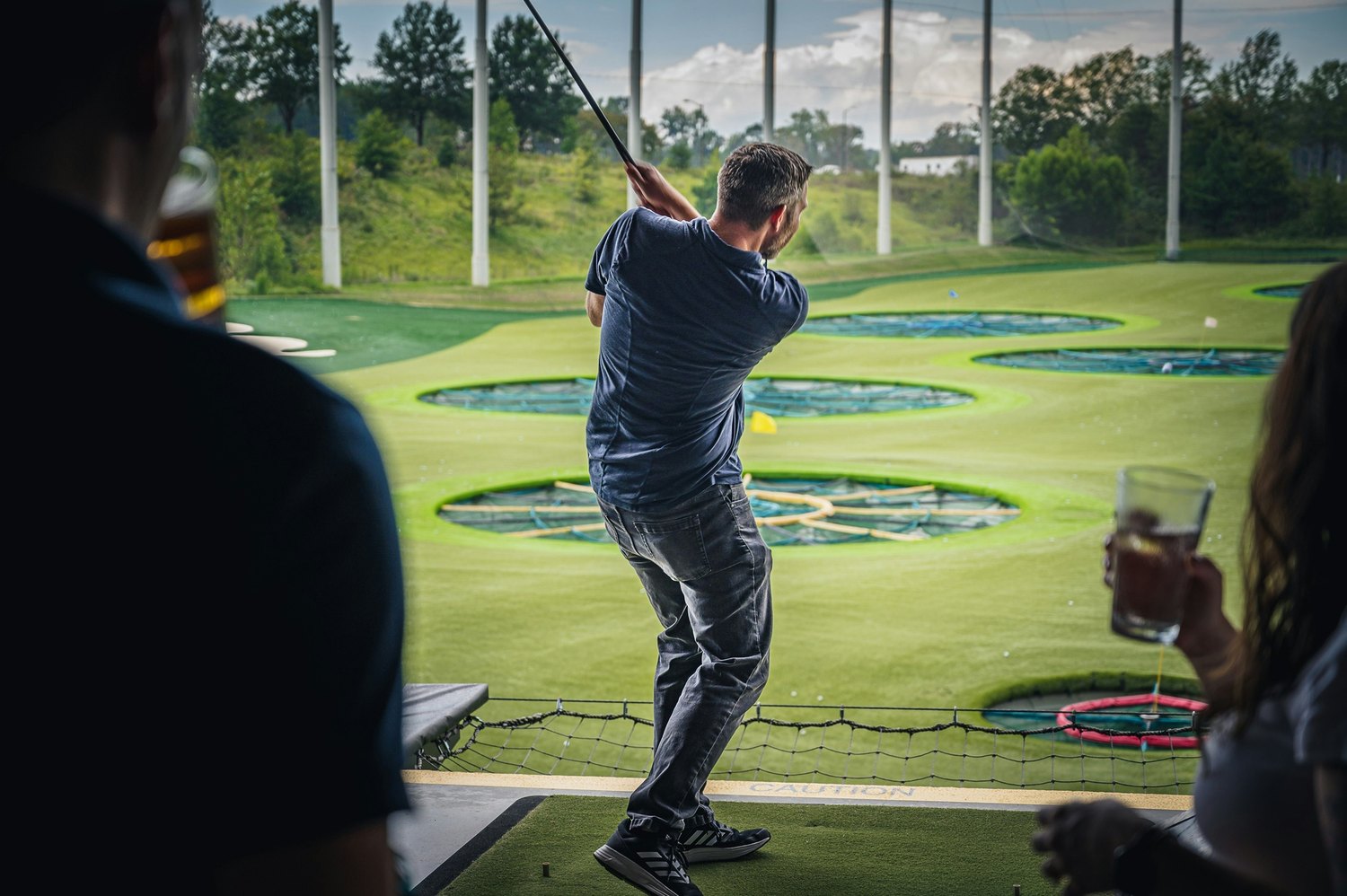 Casual golf at a driving range, with a golfer swinging and companions nearby
